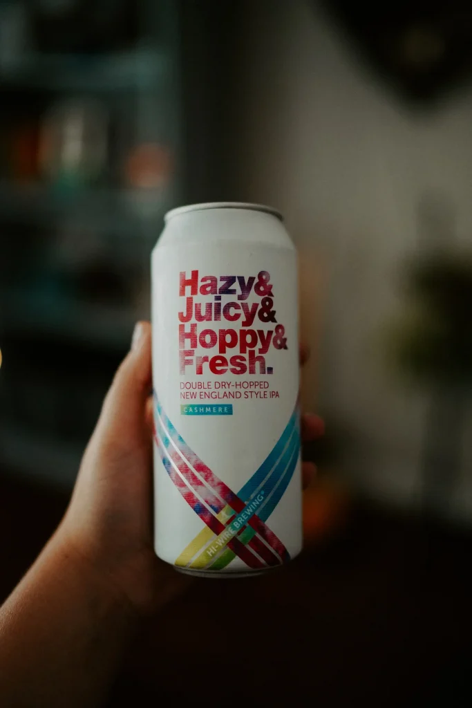 Hånd som holder en ølboks med teksten "Hazy & Juicy & Hoppy & Fresh.", en dobbel tørrhumlet New England IPA fra Hi-Wire Brewing med Cashmere-humle.