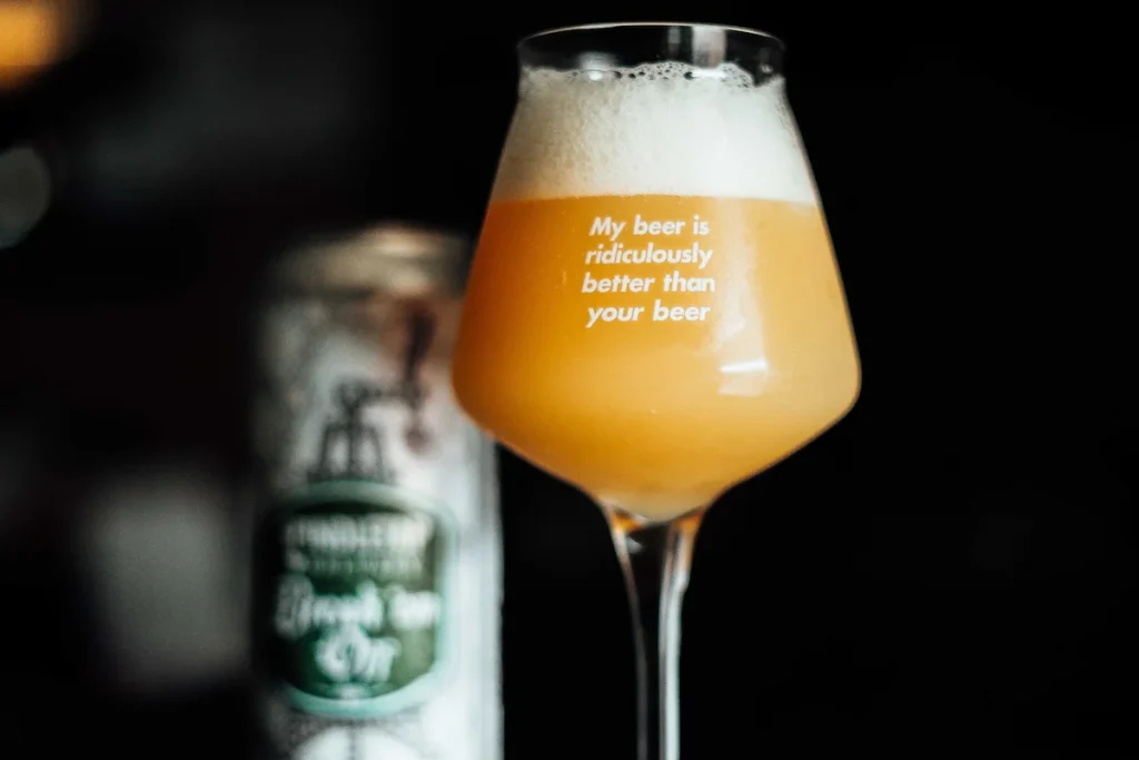 Tåkete og fyldig New England IPA i et elegant ølglass med teksten "My beer is ridiculously better than your beer", med en ølboks i bakgrunnen mot mørk bakgrunn.