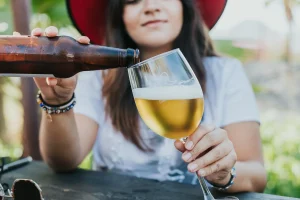 En kvinne med hatt som fyller øl fra en brun flaske i et glass med stett.