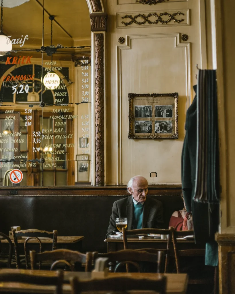 En gammel mann på en cafe i belgia med et øl i glasset foran seg